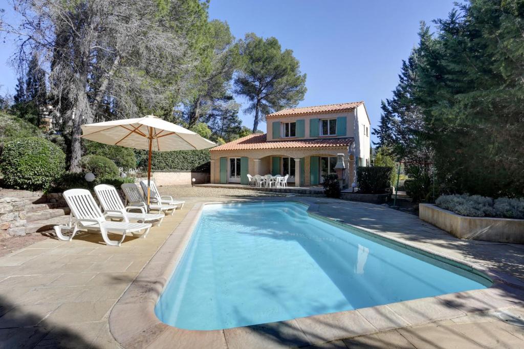 een zwembad met stoelen en een parasol en een huis bij villa 8 pers, climatisée, piscine chauffée, un havre de paix sous les pins parasols in Roquebrune-sur-Argens