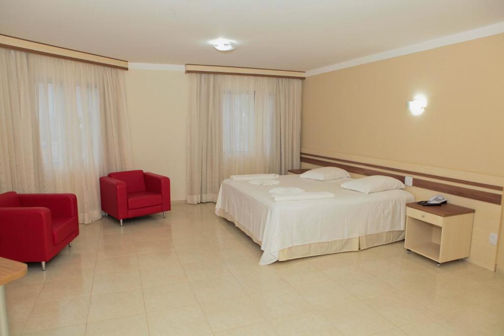 グアラプアバにあるSan Marino Palace Hotelのベッドルーム1室(ベッド1台、赤い椅子2脚付)