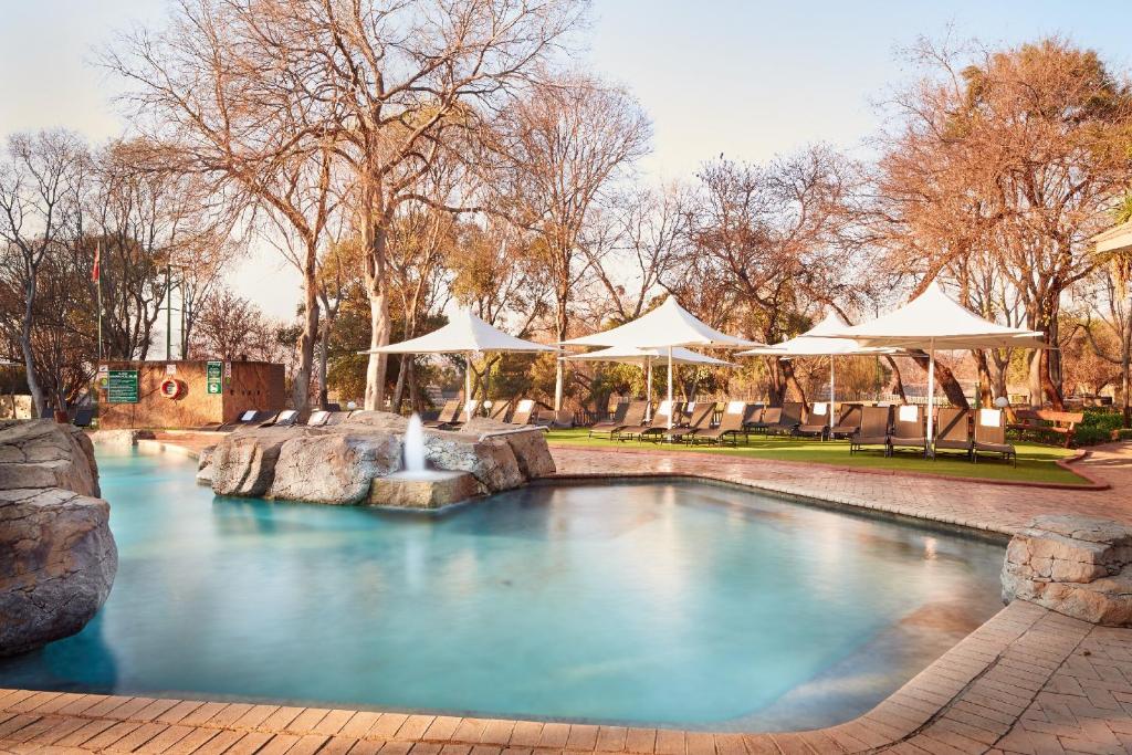 a pool with a waterfall in a park with umbrellas at First Group Magalies Park in Hartbeespoort