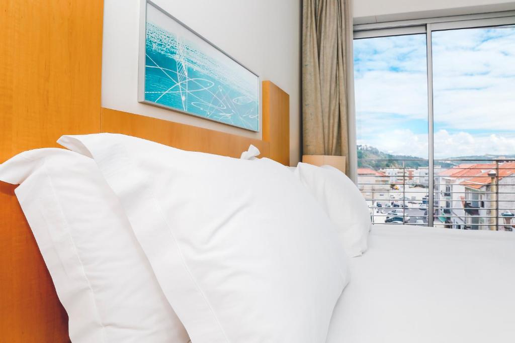 a bedroom with a white bed and a window at Hotel Praia in Nazaré