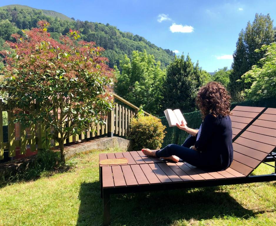 a woman sitting on a bench reading a book at casa rural casa cerezal in Cangas de Onís