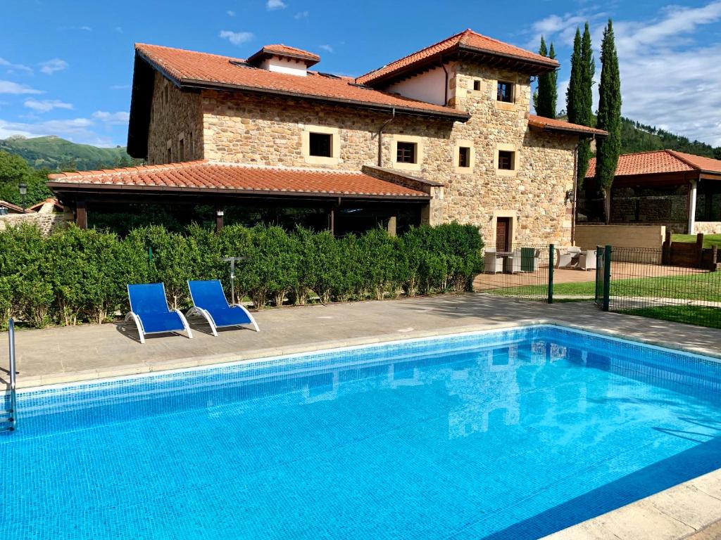 - une piscine avec deux chaises bleues en face d'une maison dans l'établissement Akla Hotel Suites Valles Pasiegos, à Saro