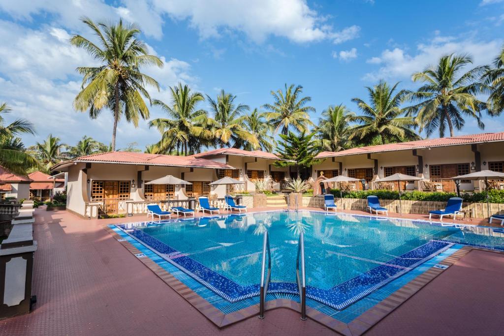 a view of a resort pool with chairs and palm trees at Leoney Resort Goa in Vagator