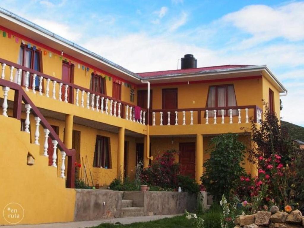 a yellow house with a balcony and flowers at Hostal Utama in Comunidad Yumani