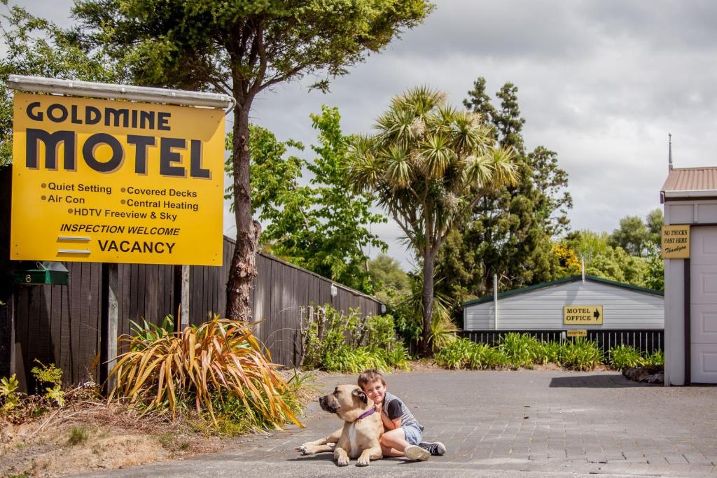 un garçon et un chien assis à côté d'un panneau dans l'établissement Goldmine Motel, à Waihi
