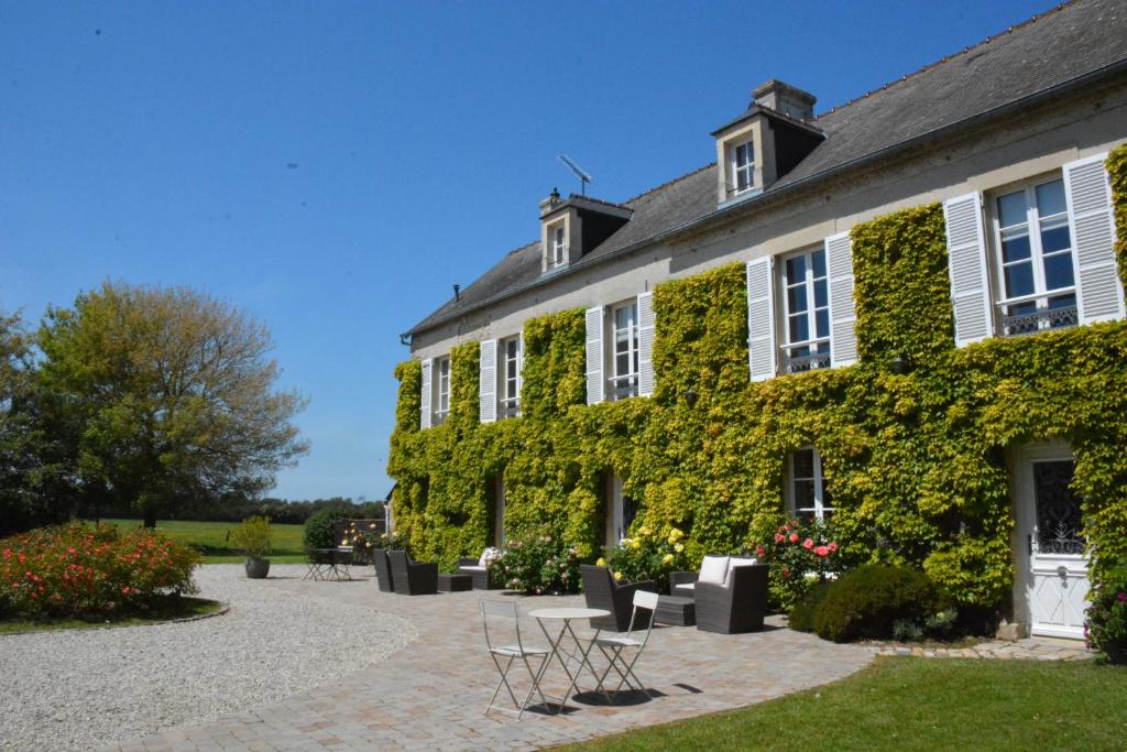 un edificio cubierto de hiedra con sillas delante en Chambres d'Hôtes Les Chaufourniers, en Crouay