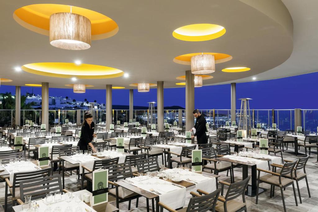a restaurant with white tables and chairs and two people walking around at Hotel Riu Vistamar Gran Canaria - All Inclusive in Puerto Rico de Gran Canaria