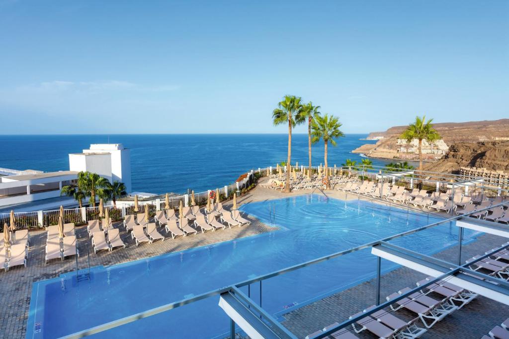 a swimming pool with chairs and the ocean at Hotel Riu Vistamar Gran Canaria - All Inclusive in Puerto Rico de Gran Canaria