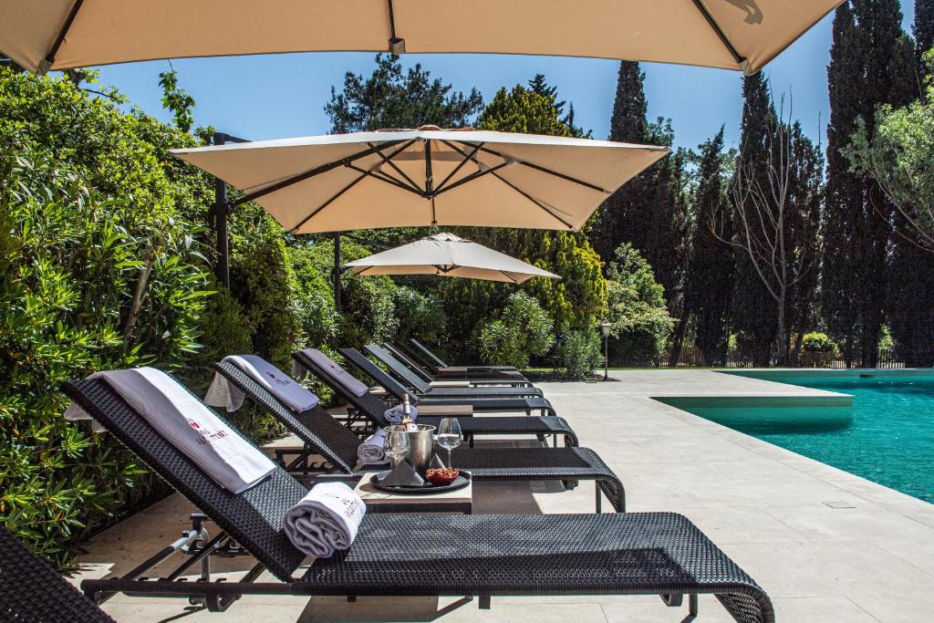 a row of lounge chairs with umbrellas next to a pool at Hôtel Mas Valentine in Saint-Rémy-de-Provence