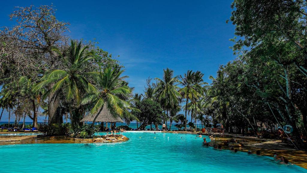 uma grande piscina com palmeiras e o oceano em Papillon Lagoon Reef Hotel em Diani Beach