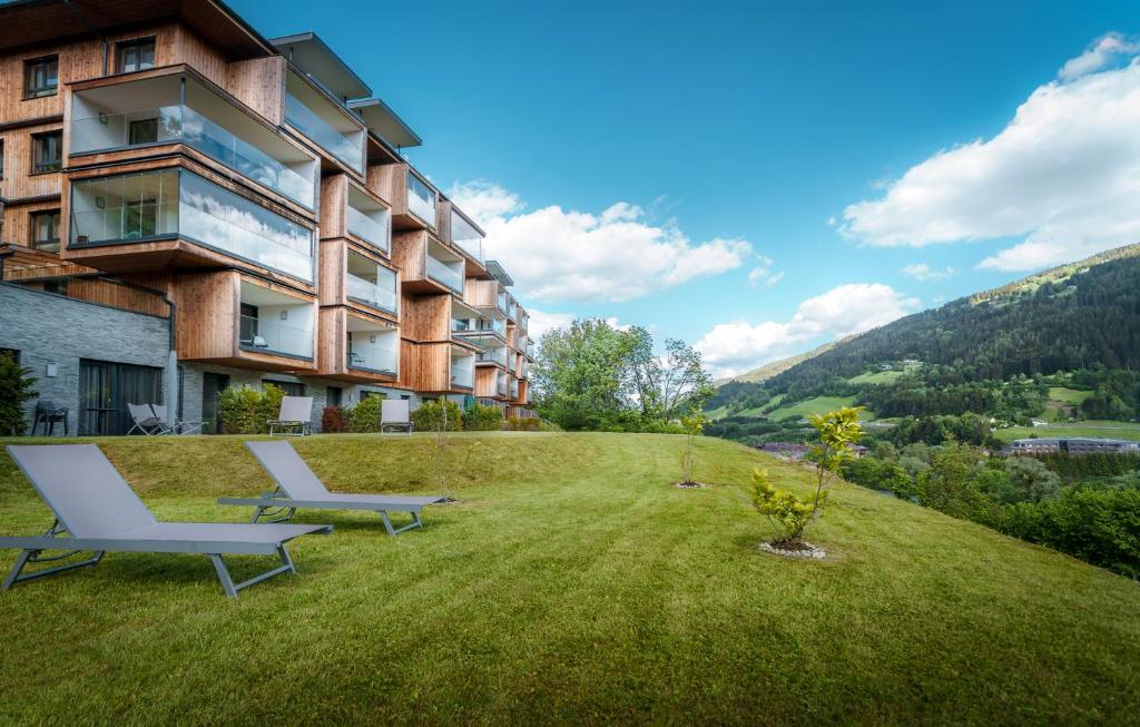 a building on a grassy hill with two lounge chairs at Sun Lodge Schladming by Schladming-Appartements in Schladming