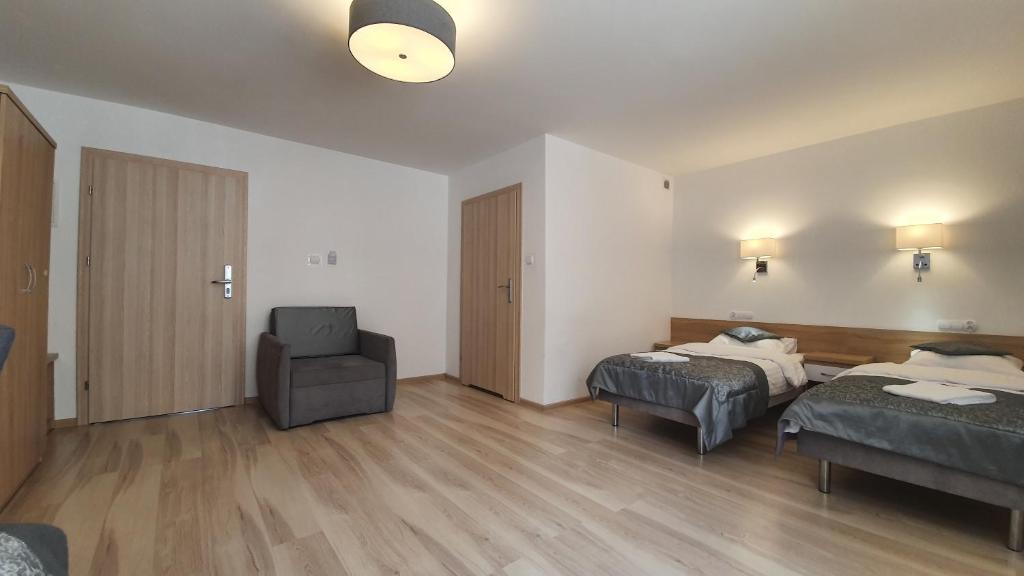 Room with two beds, armchair, wooden floor, and closed doors.