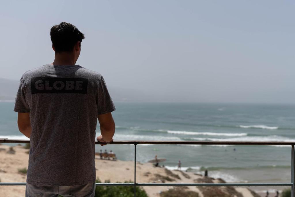 un uomo in piedi su un balcone che guarda la spiaggia di Imsouane Surf Paradise a Imsouane