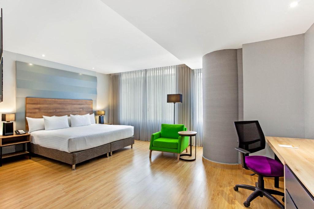 a hotel room with a bed and a green chair at La Quinta by Wyndham Medellin in Medellín