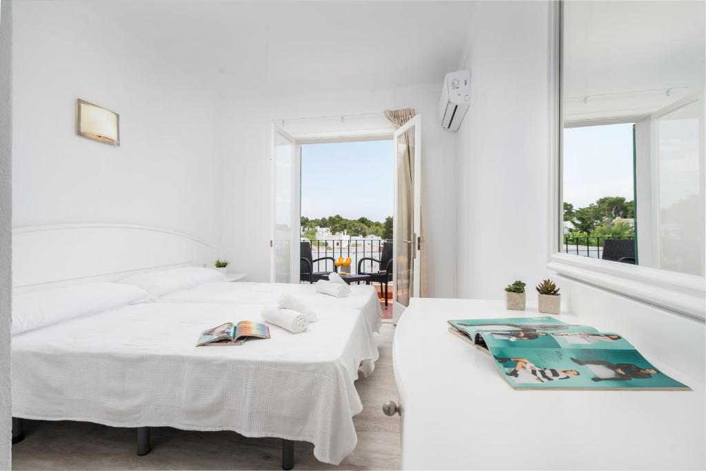 a white bedroom with two beds and a window at Hostal Talamanca in Cala d´Or