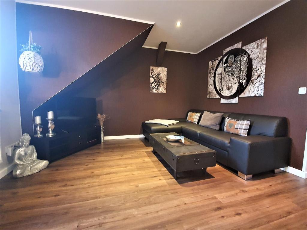 a living room with a black leather couch and a staircase at Ferienwohnung Jamie in Ostseebad Karlshagen