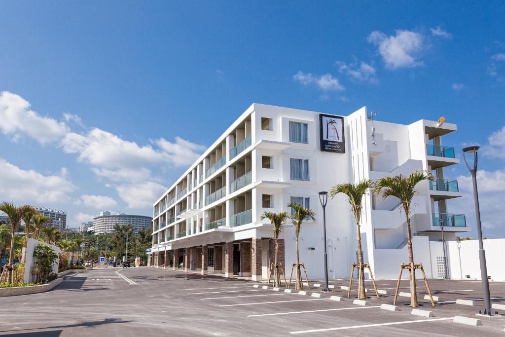 ein weißes Gebäude mit Palmen auf einem Parkplatz in der Unterkunft Kariyushi LCH. Resort in Nago