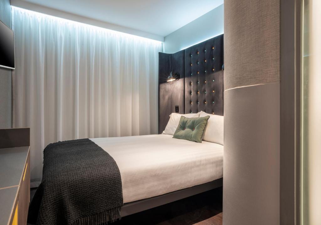 a bedroom with a bed with white sheets and green pillows at Point A Hotel London Paddington in London