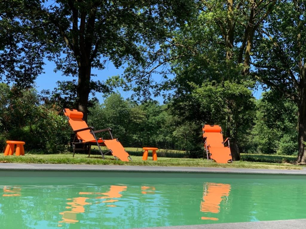 dos sillas naranjas sentadas junto a una piscina de agua en The Annex Retreat - a luxury countryside villa en Geysteren