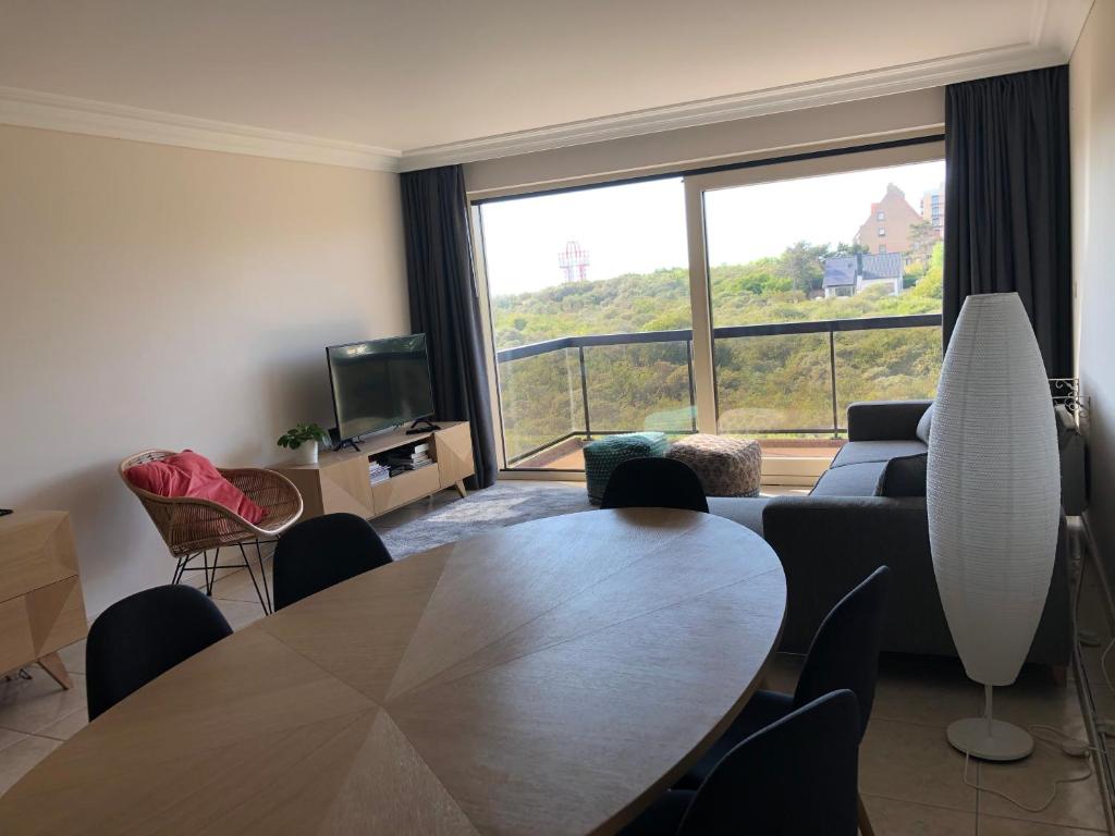 een woonkamer met een tafel en een groot raam bij Ruim 3 slaapkamerappartement vlakbij het strand in Koksijde