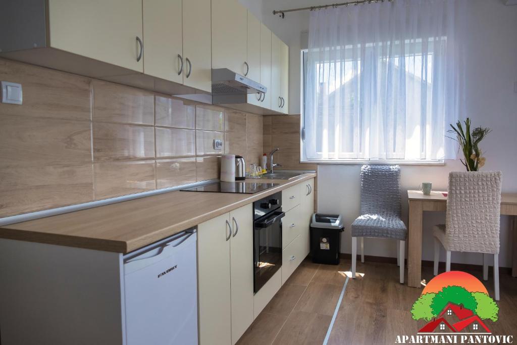 a kitchen with white cabinets and a table with a chair at Apartmani Pantovic - Apartman 1 in Trebinje