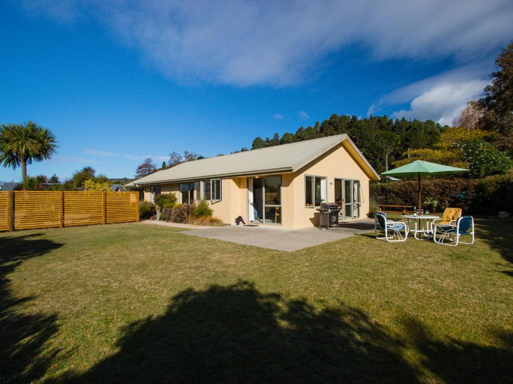 uma pequena casa com uma mesa e um guarda-chuva verde em Tasman Treat - Marahau Holiday Home em Marahau