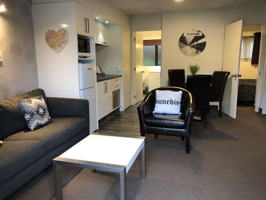 a living room with a couch and chairs and a kitchen at Commodore Motel in Dunedin