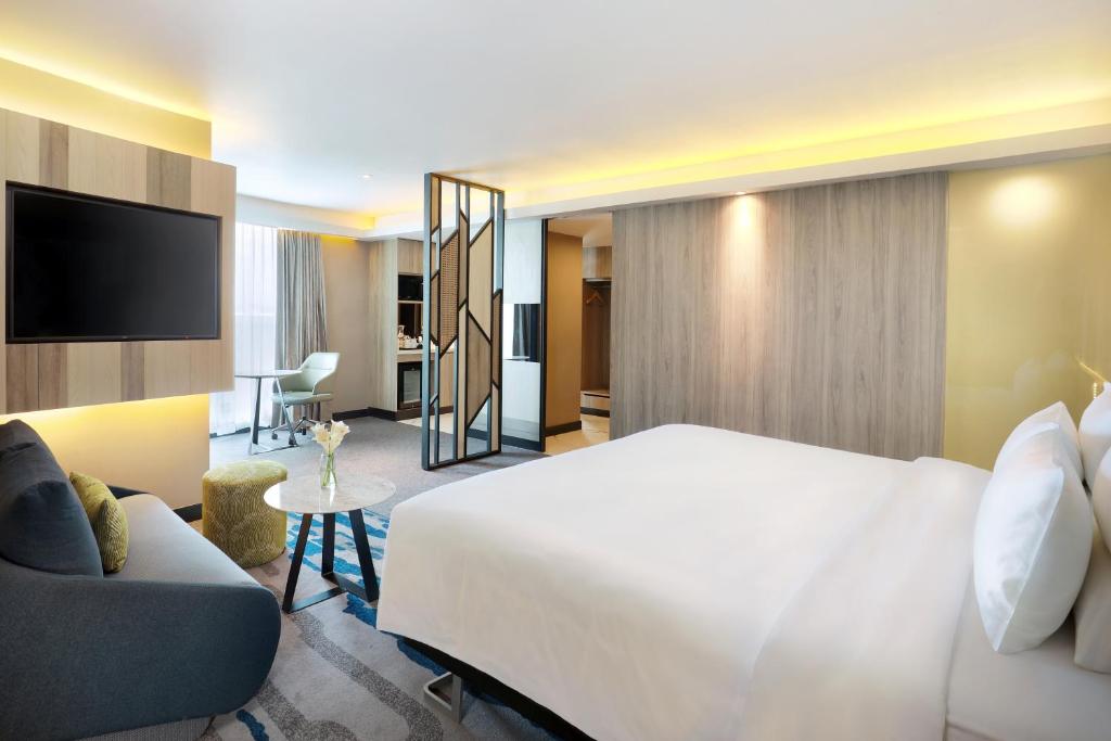 a hotel room with a bed and a couch and a tv at Novotel Suites Yogyakarta Malioboro in Yogyakarta