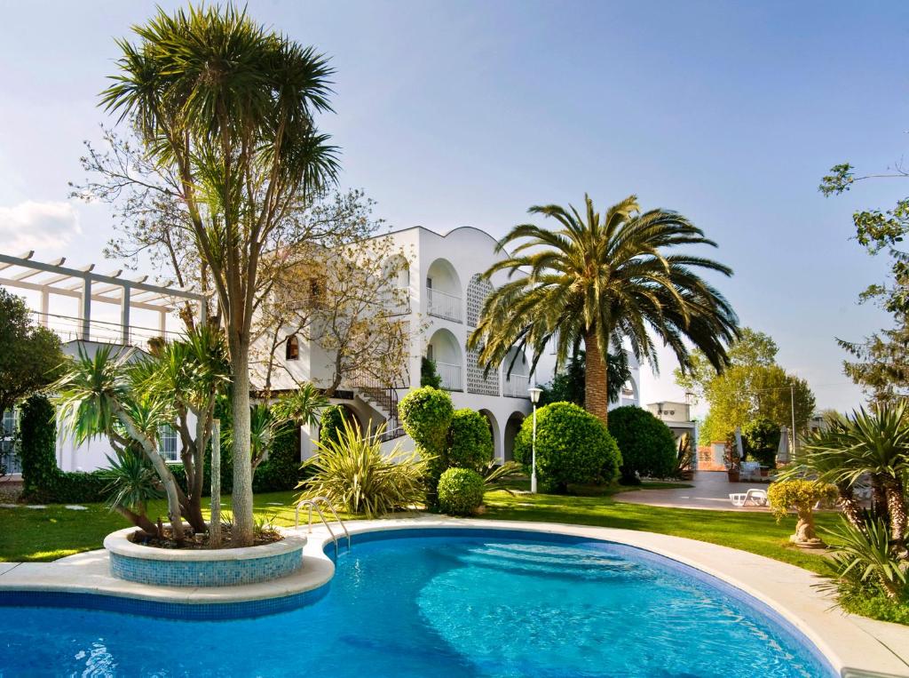 a swimming pool in front of a house with palm trees at Hotel El Molí in Sant Pere Pescador