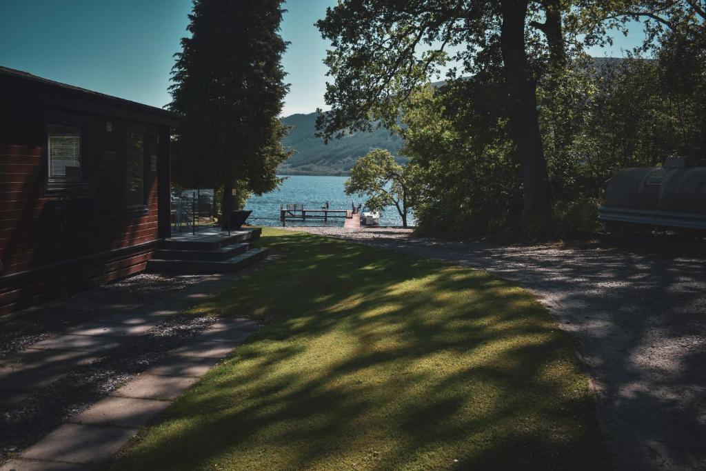 a house with a shady lawn next to a lake at Lodge at Loch Lomond in Glasgow