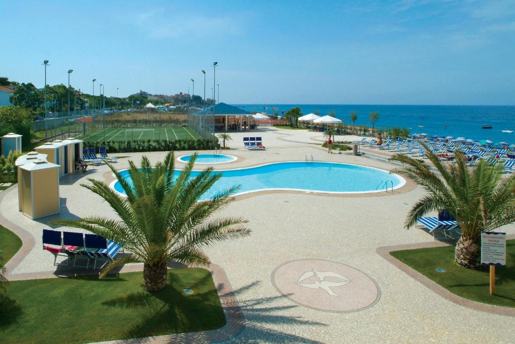 a resort swimming pool with palm trees and the ocean at Hotel dei Focesi in Diamante