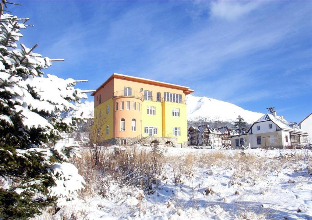 ein großes gelbes Gebäude auf einem schneebedeckten Feld in der Unterkunft Lydia in Vysoké Tatry