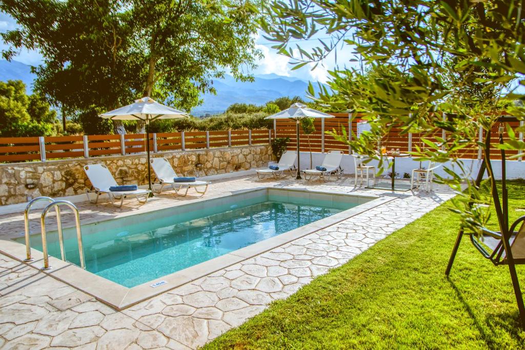 a swimming pool in a yard with chairs and umbrellas at Villa Archontiki I - Private Pool in Vryses