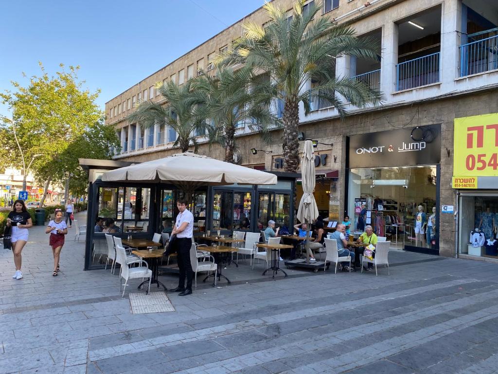 een groep mensen die aan tafels buiten een winkel zitten bij Eden Hotel in Haifa