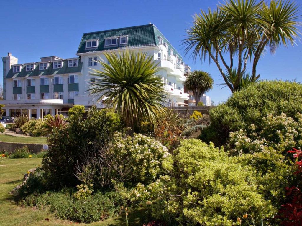 a large white building with palm trees and bushes at Bournemouth East Cliff Hotel, Sure Hotel Collection by BW in Bournemouth