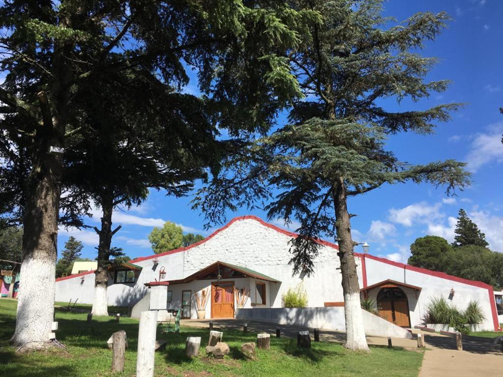 Un granero blanco con dos árboles delante. en Portal de La Cumbre en La Cumbre