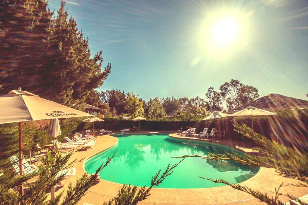 una piscina con sillas y sombrillas en un día soleado en Pao Pao Lodge Algarrobo en Algarrobo