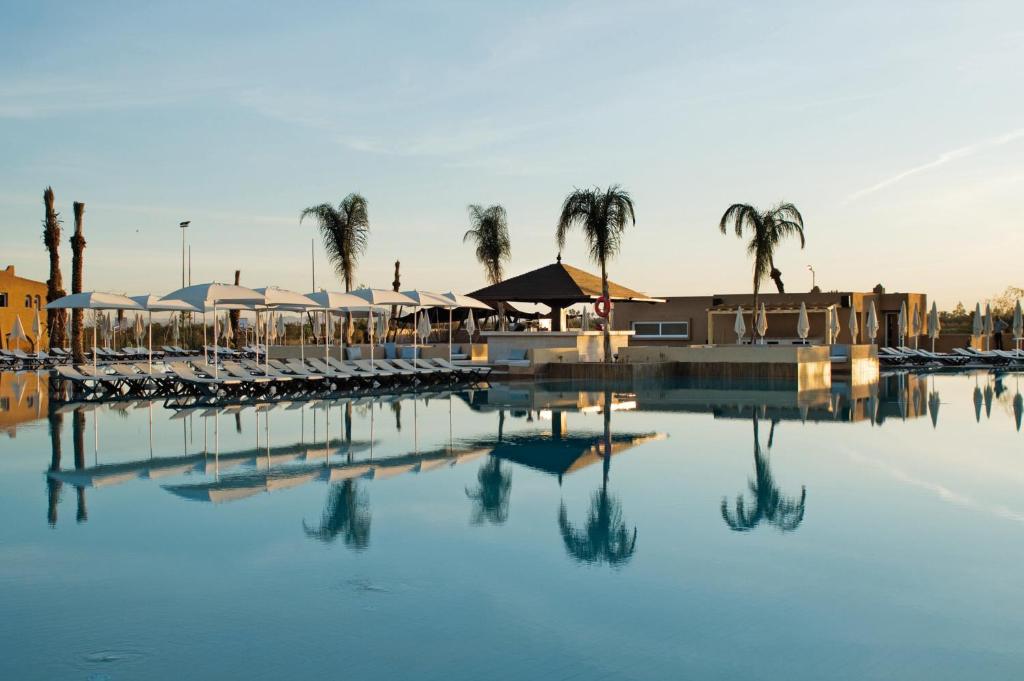 a pool of water with chairs and palm trees at Hotel Riu Tikida Palmeraie - All Inclusive in Marrakech