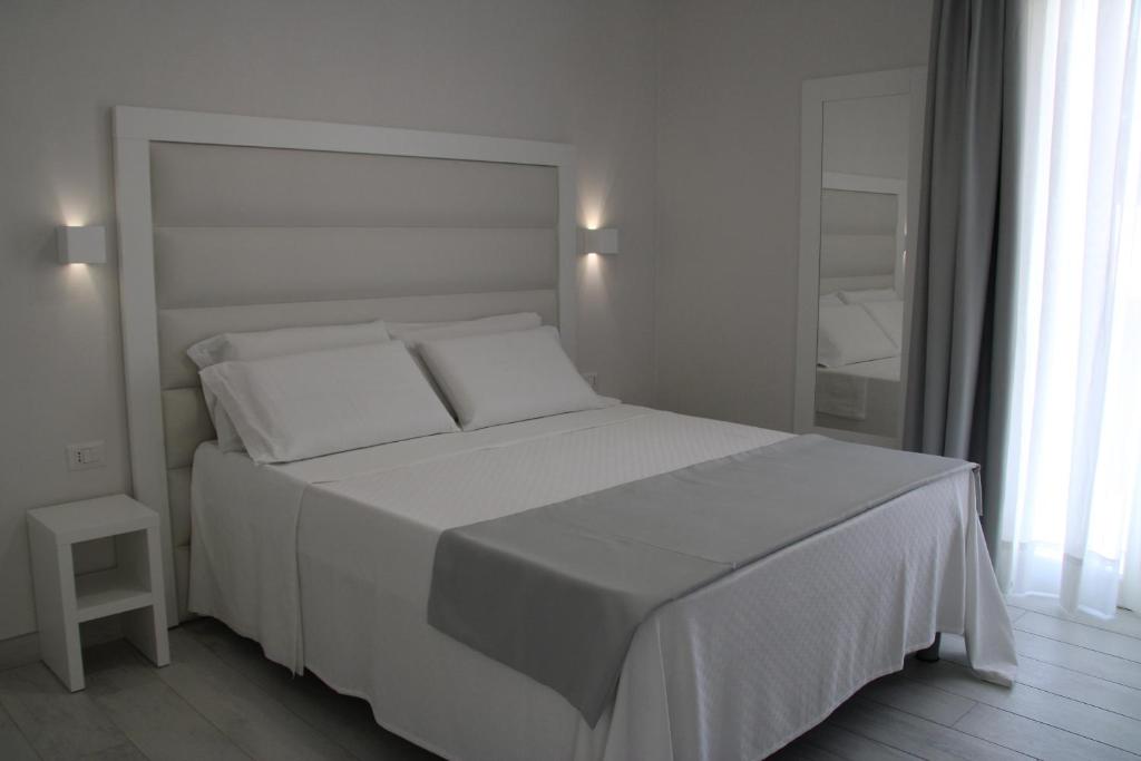 Dormitorio blanco con cama blanca y espejo en La Guitgia Rooms, en Lampedusa