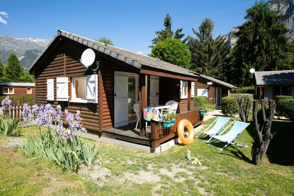 une petite cabane en rondins avec une chaise et des fleurs dans l'établissement A La Rencontre Du Soleil - Camping, au Bourg-dʼOisans