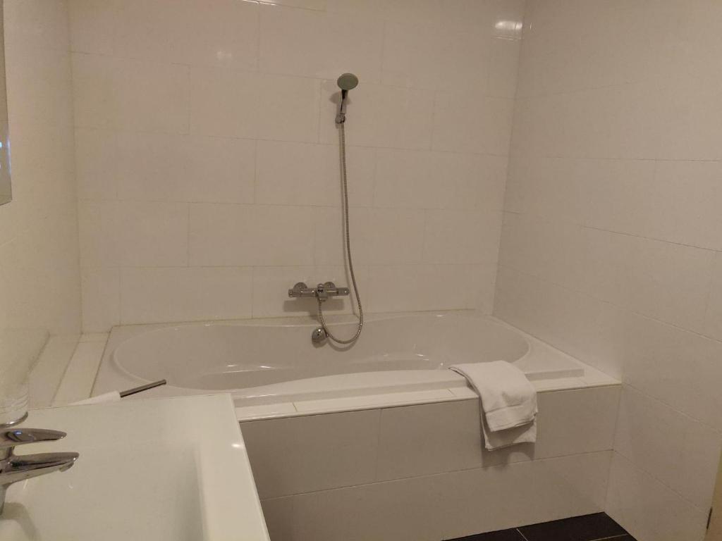 a white bathroom with a bath tub with a shower at Hotel Johannes Vermeer Delft in Delft