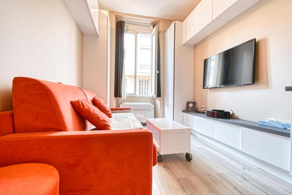 Il comprend un salon avec une chaise orange et une télévision à écran plat. dans l'établissement Beautiful and cozy apartment in the heart of Cannes, à Cannes