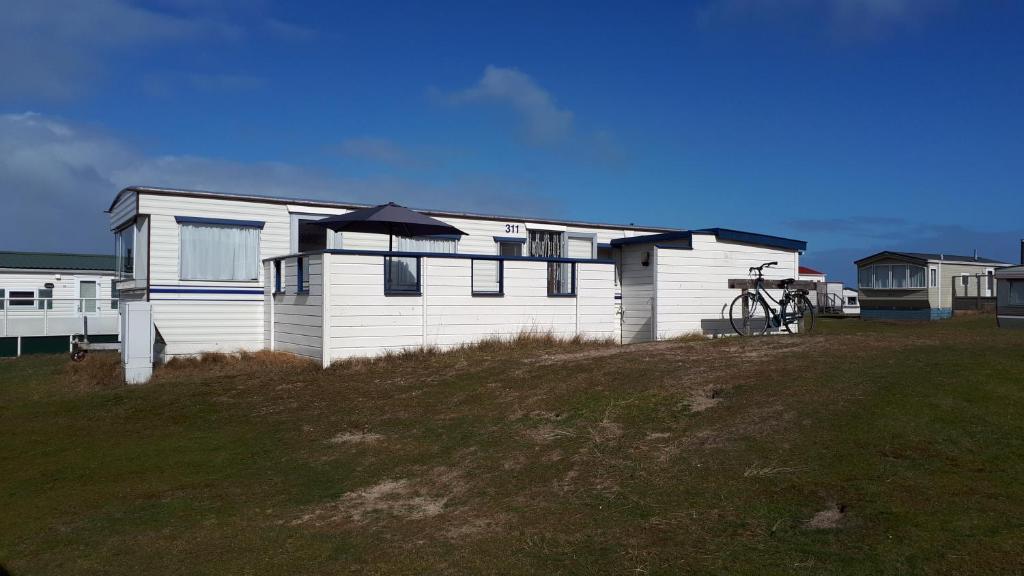 a white house sitting on top of a grassy hill at AMELAND - Ballum: Stacaravan Chalet (incl. fietsen) bij strand en zee in Ballum