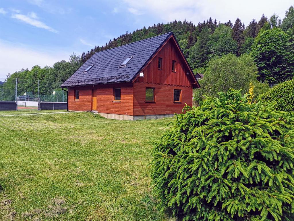 a red house with a black roof in a field at Apartmány Ski areal Kareš in Loučná nad Desnou