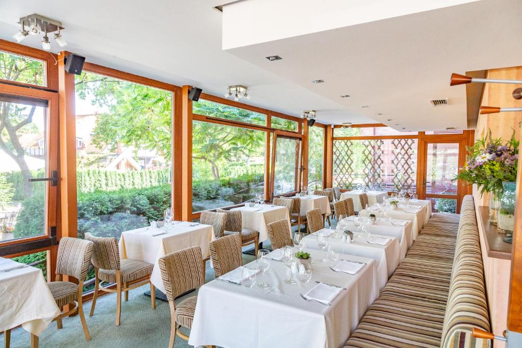 a restaurant with white tables and chairs and large windows at Nerija in Nida