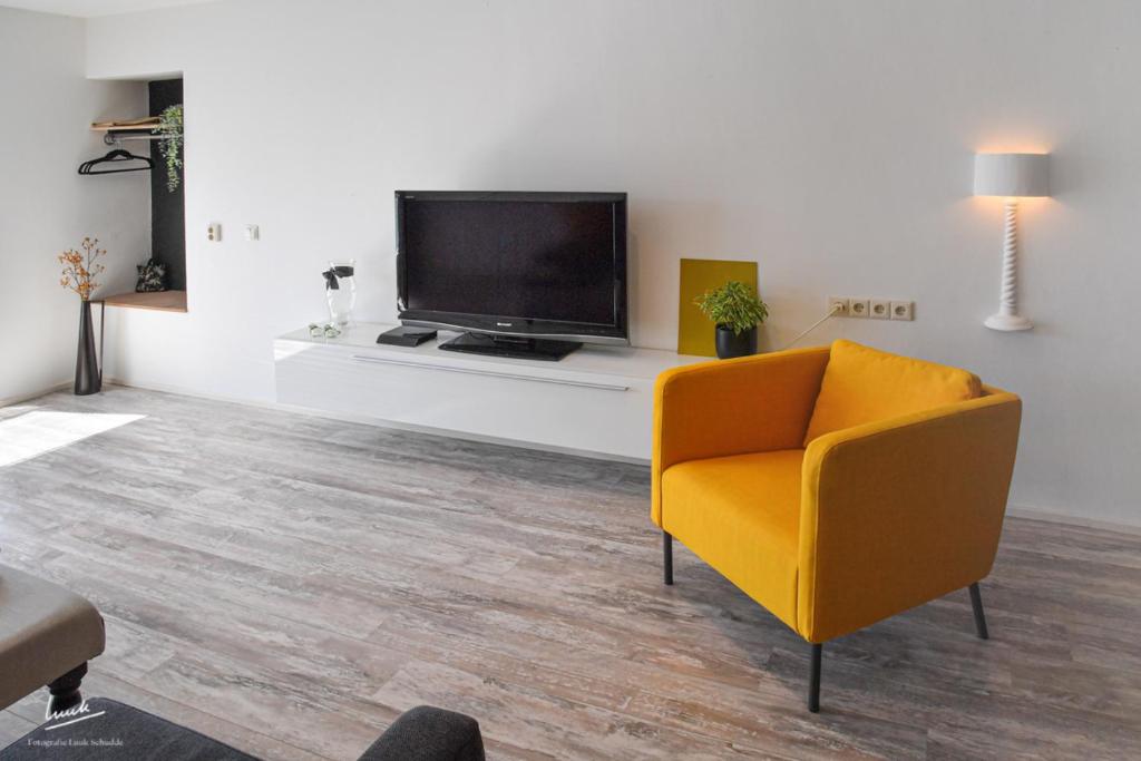 ein Wohnzimmer mit einem gelben Stuhl und einem TV in der Unterkunft Hofstee appartement. in Urk