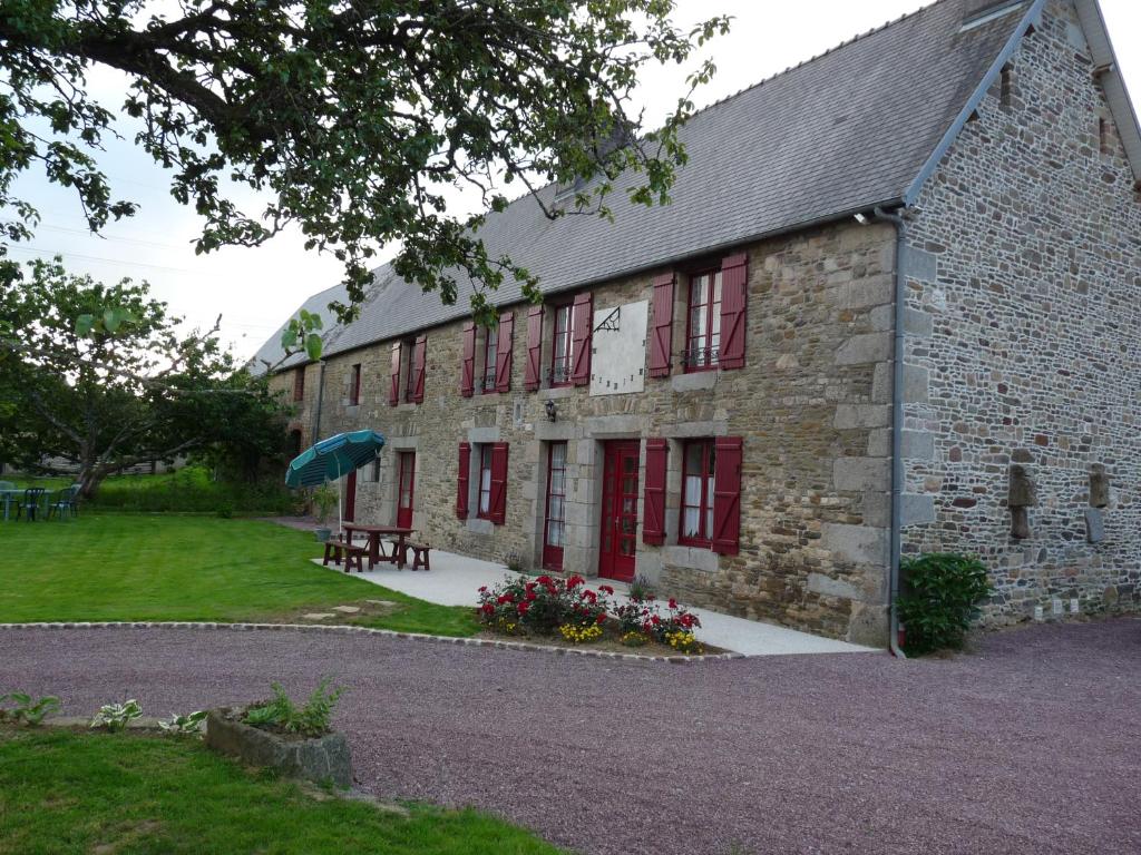 un edificio de piedra con ventanas rojas y una mesa con sombrilla en gite Le verger de la Faverie, en Saint-Nicolas-des-Bois
