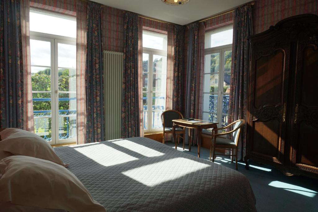 a bedroom with a bed and chairs and windows at Hotel La Diligence in Honfleur