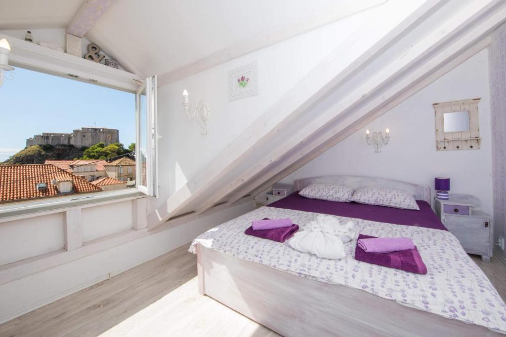 sypialnia z łóżkiem z fioletowymi poduszkami i oknem w obiekcie Guest House Gugily w Dubrowniku
