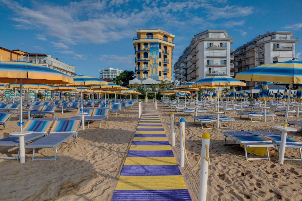 uma praia com cadeiras e guarda-sóis azuis e amarelos em Hotel Napoleon em Lido di Jesolo